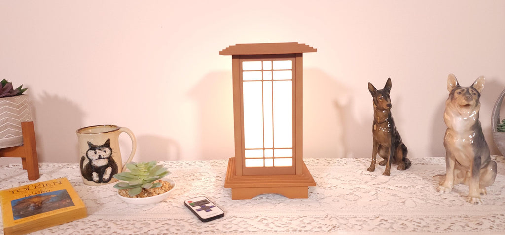 The Prairie Beacon table lantern pairs an inviting Teak wood-tone finish with the sculptural elegance of American-inspired architecture. Slender corner posts, intricate geometric latticework, and translucent panels rise from a square base to a gracefully overhanging roof. Thoughtfully designed and 3D printed, its layered details create a distinctive statement piece, bringing warmth, character, and architectural beauty to a bedside table, bookshelf, or favorite corner.