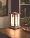 The Prairie Beacon table lantern pairs an inviting wood-tone finish with the sculptural elegance of American-inspired architecture. Slender corner posts, intricate geometric latticework, and translucent panels rise from a square base to a gracefully overhanging roof. Thoughtfully designed and 3D printed, its layered details create a distinctive statement piece, bringing warmth, character, and architectural beauty to a bedside table, bookshelf, or favorite corner.